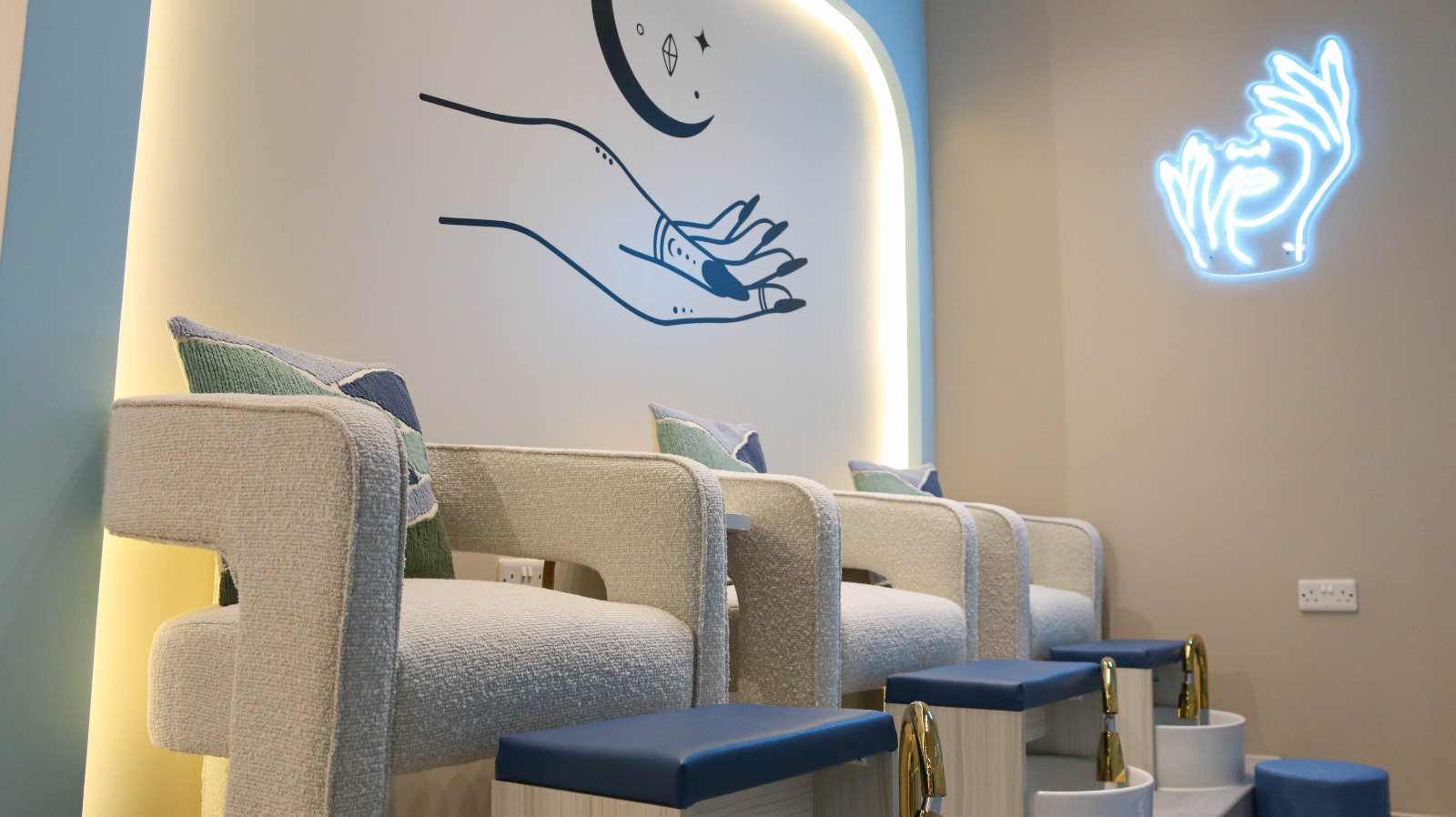 Pedicure lounge chairs with neon hand art at Qareat Al Fenjan